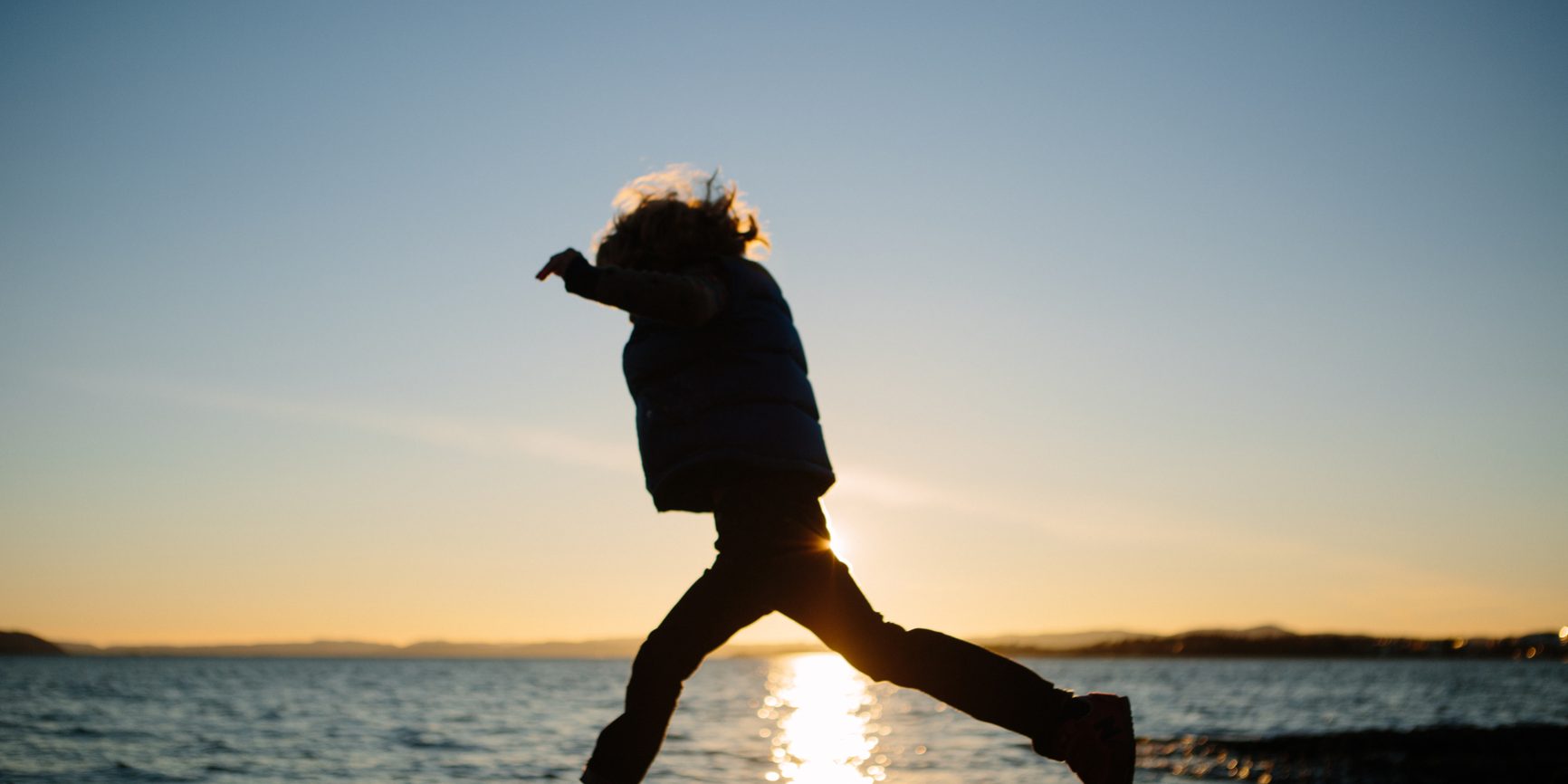 Child In Silhouette Jumps Near The Water